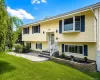 Split-level residence featuring yellow siding, dark blue shutters, and a front entry with a white railing Split-level residence featuring yellow siding, dark blue shutters, and a front entry with a white railing