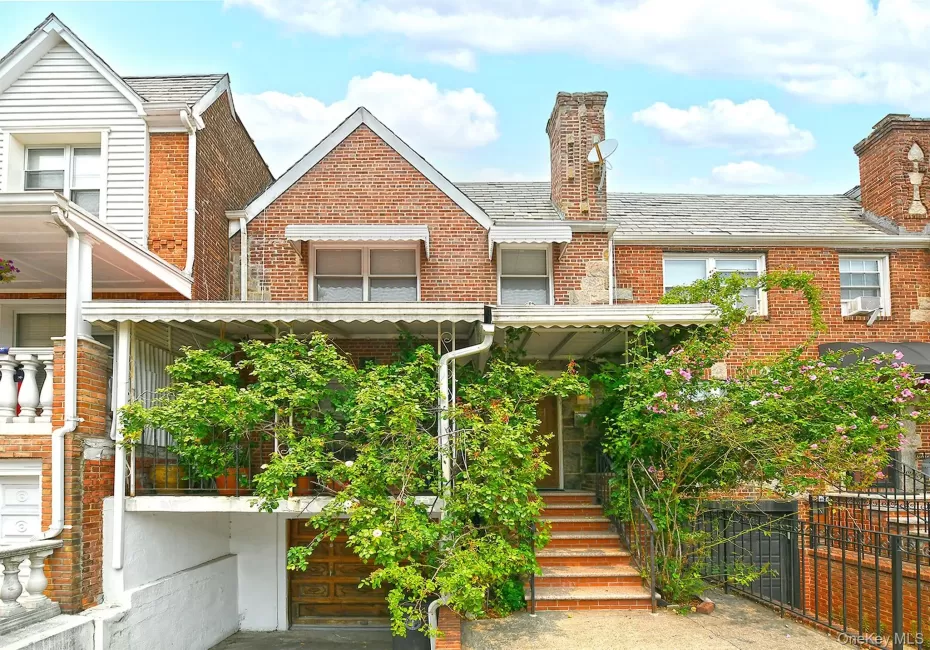 Brick facade featuring a recessed garage with a wood-finish door, a covered porch with an awning, and exterior steps leading to the entrance Brick facade featuring a recessed garage with a wood-finish door, a covered porch with an awning, and exterior steps leading to the entrance