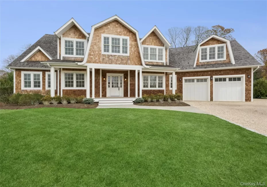Shingle-style home featuring covered porch, a front yard, a garage, driveway, and a gambrel roof Shingle-style home featuring covered porch, a front yard, a garage, driveway, and a gambrel roof