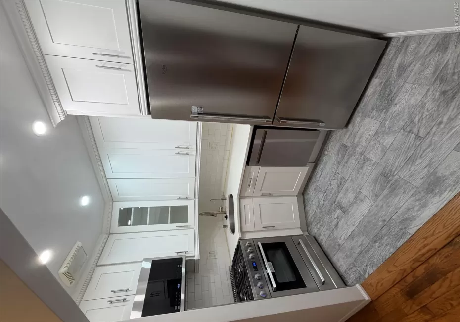 Modern kitchen featuring white shaker cabinetry, stainless steel appliances, light-toned countertops, a subway tile backsplash, and wood-finish flooring Modern kitchen featuring white shaker cabinetry, stainless steel appliances, light-toned countertops, a subway tile backsplash, and wood-finish flooring
