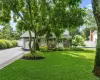Manicured front lawn with mature shade trees, paved driveway, stone facade accents, white picket fencing, and a garage with a carriage-style door Manicured front lawn with mature shade trees, paved driveway, stone facade accents, white picket fencing, and a garage with a carriage-style door