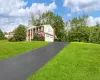 Greek revival house featuring a chimney, driveway, a garage, brick siding, and a front yard Greek revival house featuring a chimney, driveway, a garage, brick siding, and a front yard