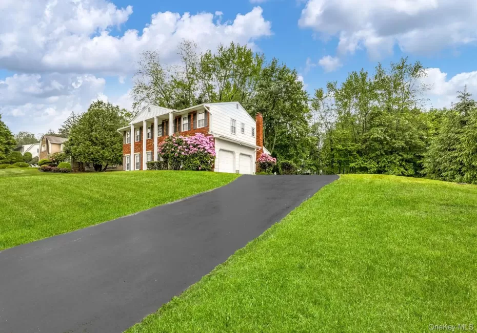 Greek revival house featuring a chimney, driveway, a garage, brick siding, and a front yard Greek revival house featuring a chimney, driveway, a garage, brick siding, and a front yard