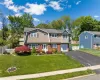 Split-level residence featuring a brick and siding facade, a manicured front lawn, a paved driveway, an attached garage, and mature landscaping Split-level residence featuring a brick and siding facade, a manicured front lawn, a paved driveway, an attached garage, and mature landscaping