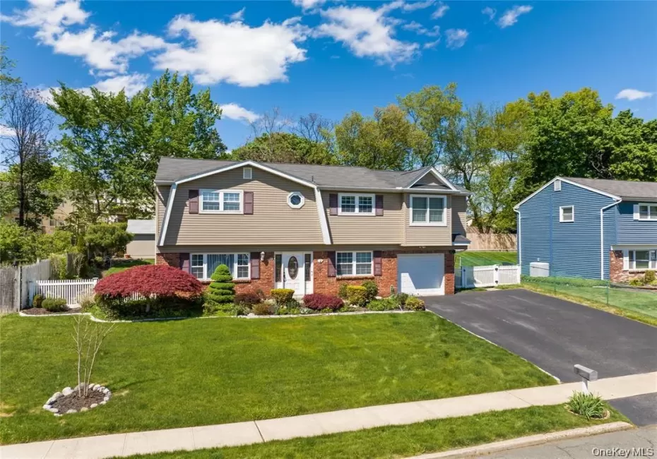 Split-level residence featuring a brick and siding facade, a manicured front lawn, a paved driveway, an attached garage, and mature landscaping Split-level residence featuring a brick and siding facade, a manicured front lawn, a paved driveway, an attached garage, and mature landscaping