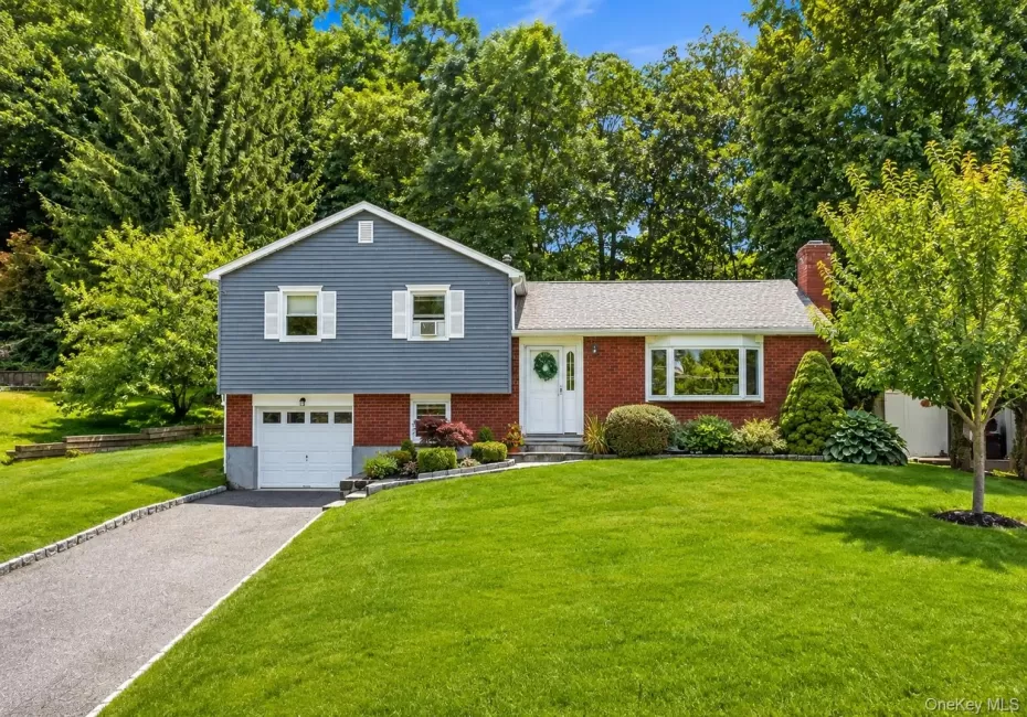 Split-level residence featuring a brick and blue siding exterior, an attached single-car garage, and a paved driveway Split-level residence featuring a brick and blue siding exterior, an attached single-car garage, and a paved driveway