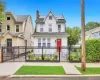 White two-story residence featuring a prominent red entry door, an ornate black metal fence, and solar panels White two-story residence featuring a prominent red entry door, an ornate black metal fence, and solar panels