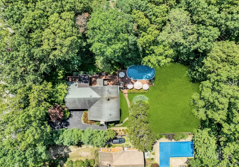 Aerial view of this home's expansive outdoor living space featuring a resort-style pool with surrounding lounge seating, manicured lawn, mature tree-lined perimeter, and multiple entertaining areas adjacent to the residence Aerial view of this home's expansive outdoor living space featuring a resort-style pool with surrounding lounge seating, manicured lawn, mature tree-lined perimeter, and multiple entertaining areas adjacent to the residence