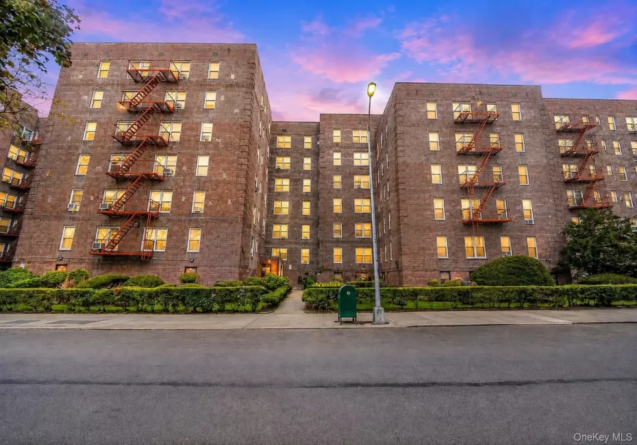 Brick multi-story building featuring multiple windows, exterior fire escapes, and ground-level landscaping Brick multi-story building featuring multiple windows, exterior fire escapes, and ground-level landscaping