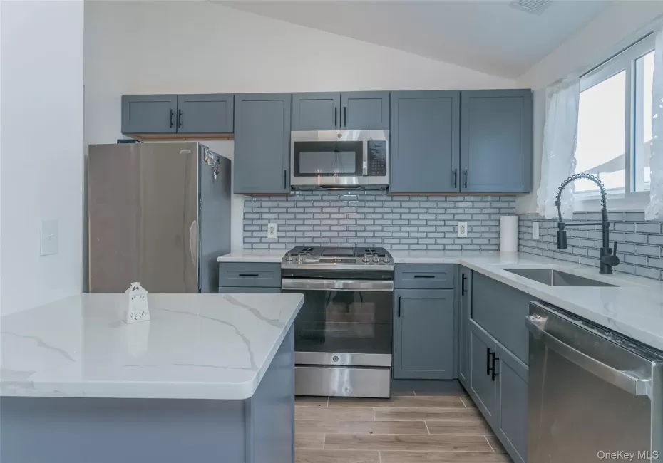 Kitchen with lofted ceiling, stainless steel appliances, light stone countertops, tasteful backsplash, and gray cabinets Kitchen with lofted ceiling, stainless steel appliances, light stone countertops, tasteful backsplash, and gray cabinets