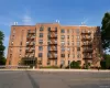 Brick multi-story building featuring multiple windows, exterior fire escapes, a glass-enclosed entrance, and surrounding shrubbery Brick multi-story building featuring multiple windows, exterior fire escapes, a glass-enclosed entrance, and surrounding shrubbery