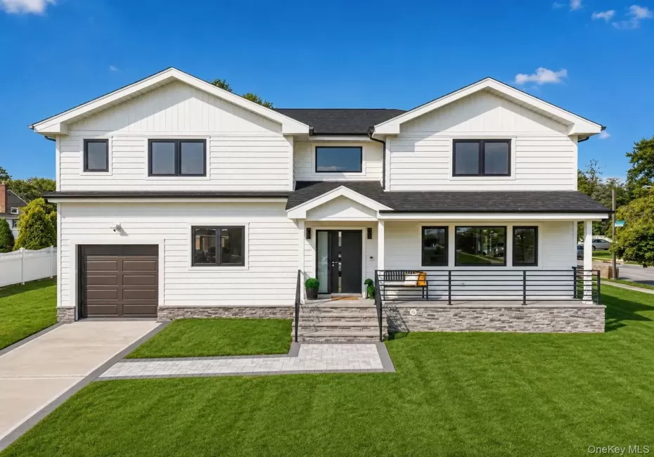 Exterior featuring white horizontal siding, black-framed windows, a covered entry with stone-clad foundation, a paved driveway, and a manicured lawn Exterior featuring white horizontal siding, black-framed windows, a covered entry with stone-clad foundation, a paved driveway, and a manicured lawn